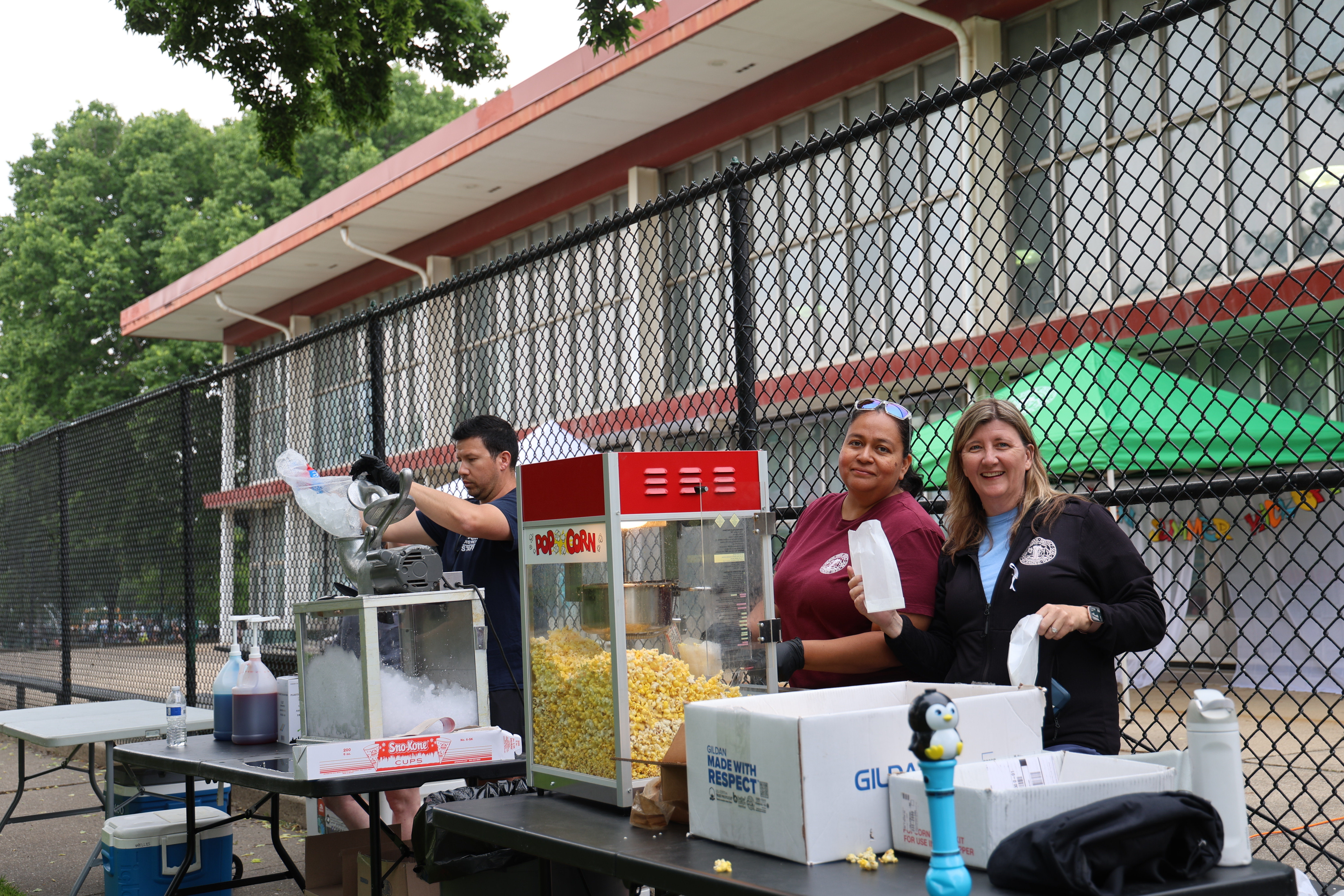 People serve popcorn and snow cones at an outdoor concession stand.